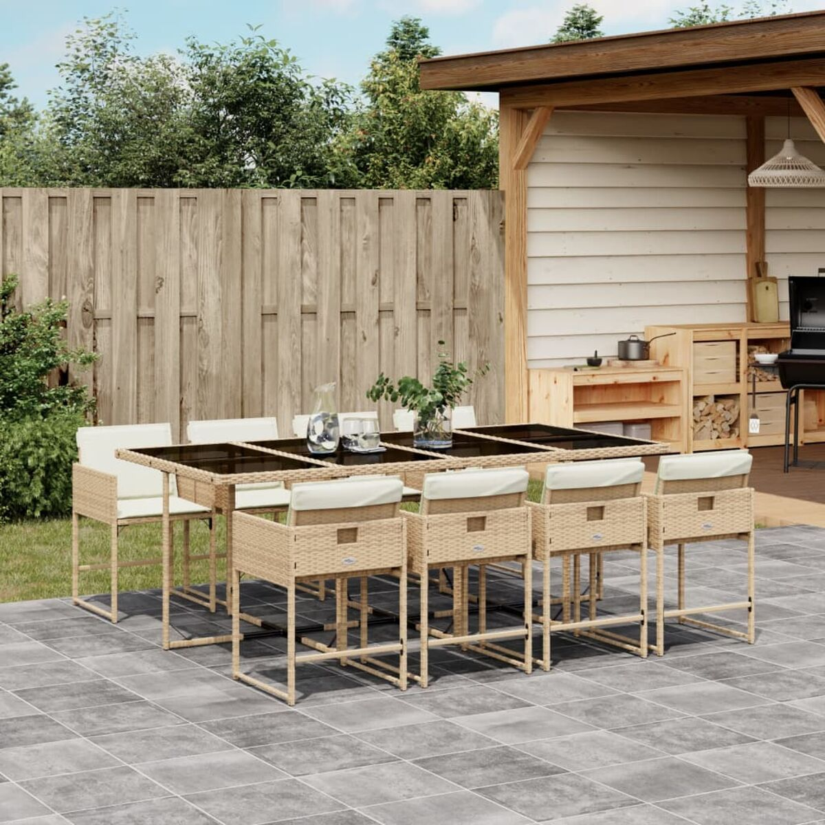 Essgruppe im Freien: rechteckiger Tisch mit Glasplatte und Korbstühlen, auf gefliester Terrasse, sonniger Tag.
