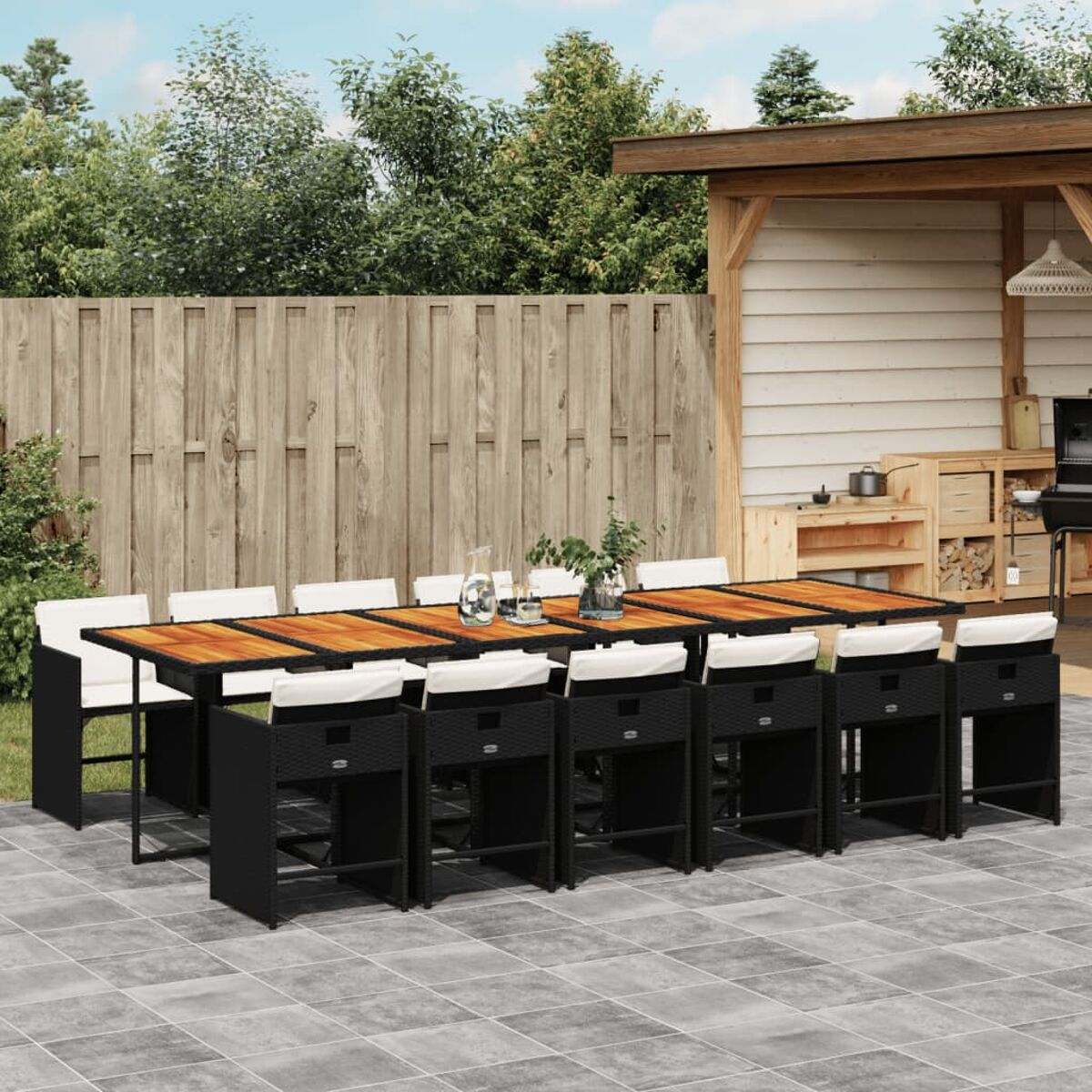 Essgruppe im Freien. Ein Tisch mit Stühlen auf einer Terrasse mit Holzzaun und Bäumen.