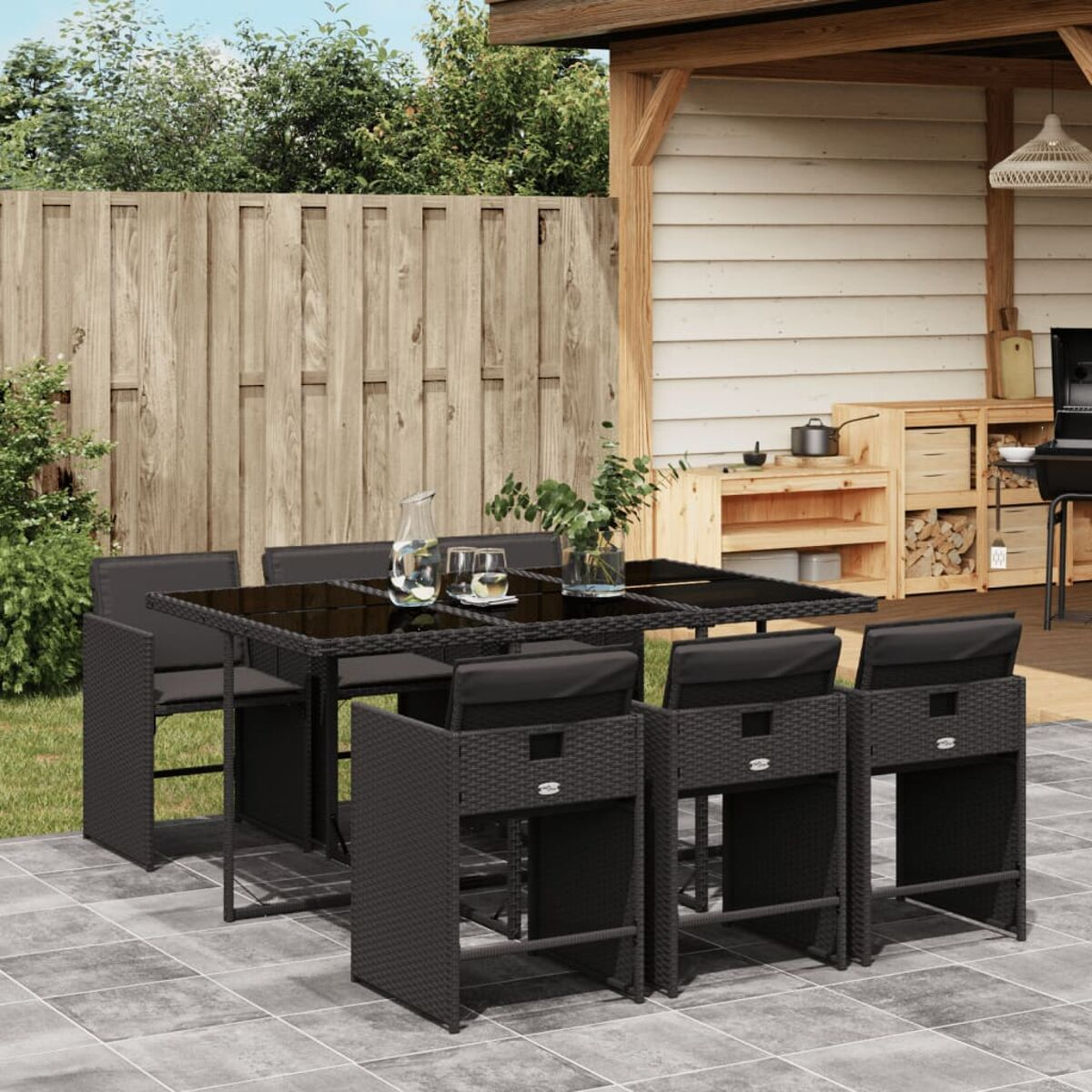 Schwarzes Wicker-Terrassenmöbel mit Tisch, sechs Stühlen und schwarzen Kissen, in einem Garten.