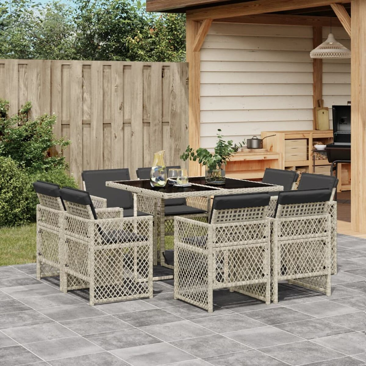 Set da pranzo all'aperto. Sedie beige intrecciate con cuscini neri attorno a un tavolo di vetro. Patio pavimentato.