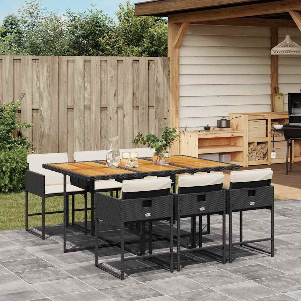 Un set da pranzo all'aperto con tavolo in legno, sedie e accessori. Si vedono vegetazione e pannelli di legno.