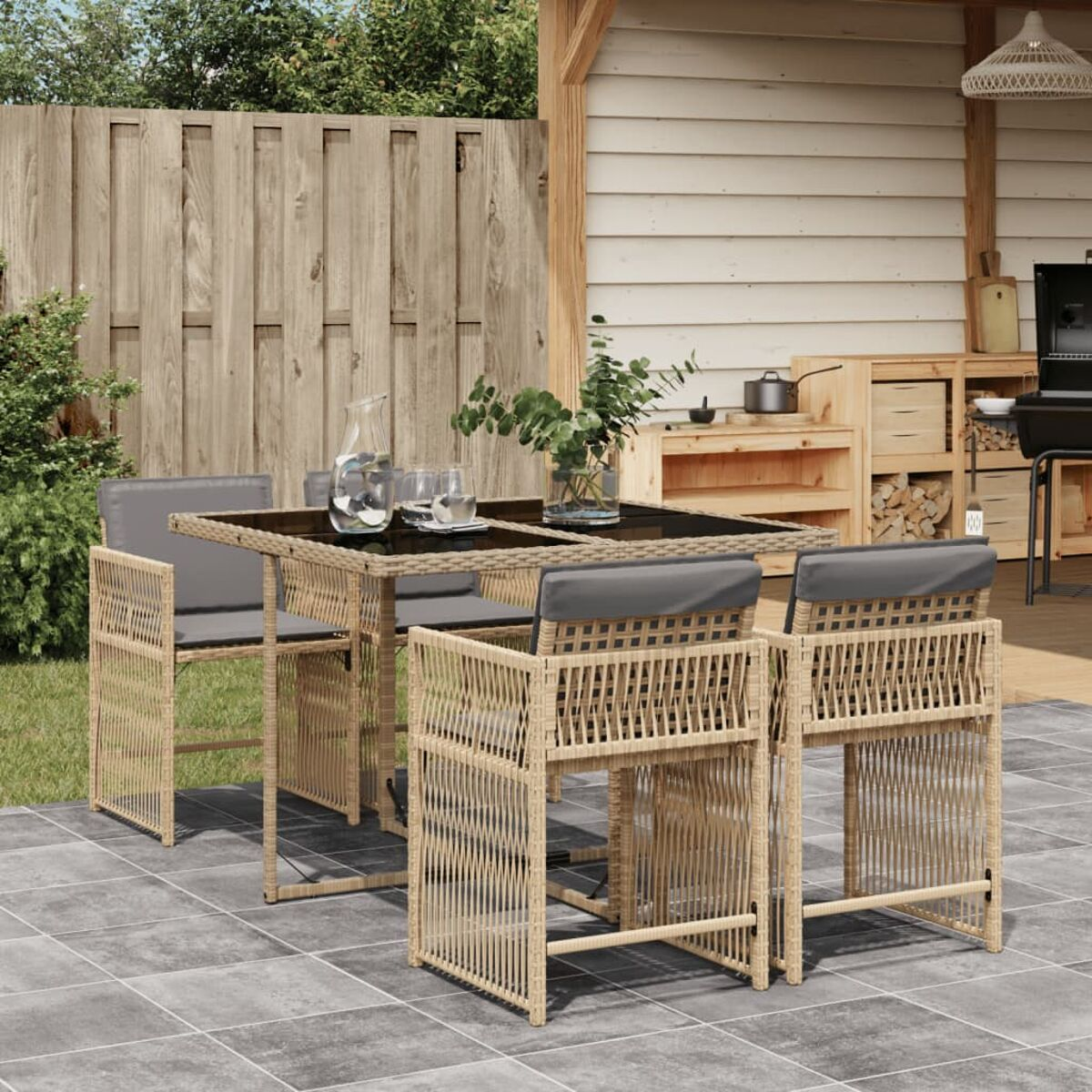 Set da patio esterno con tavolo, sedie, piante e una staccionata in legno sullo sfondo.