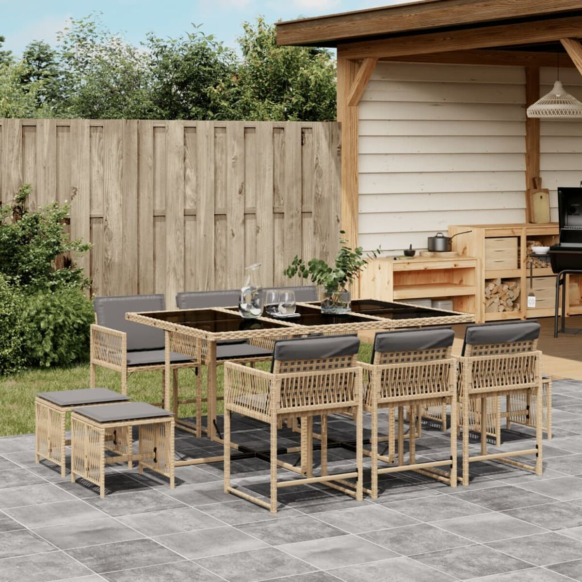 Essgarnitur im Freien: Tisch, Stühle und Hocker. Korbmöbel, graue Kissen, Holzterrasse und ein Zaun.