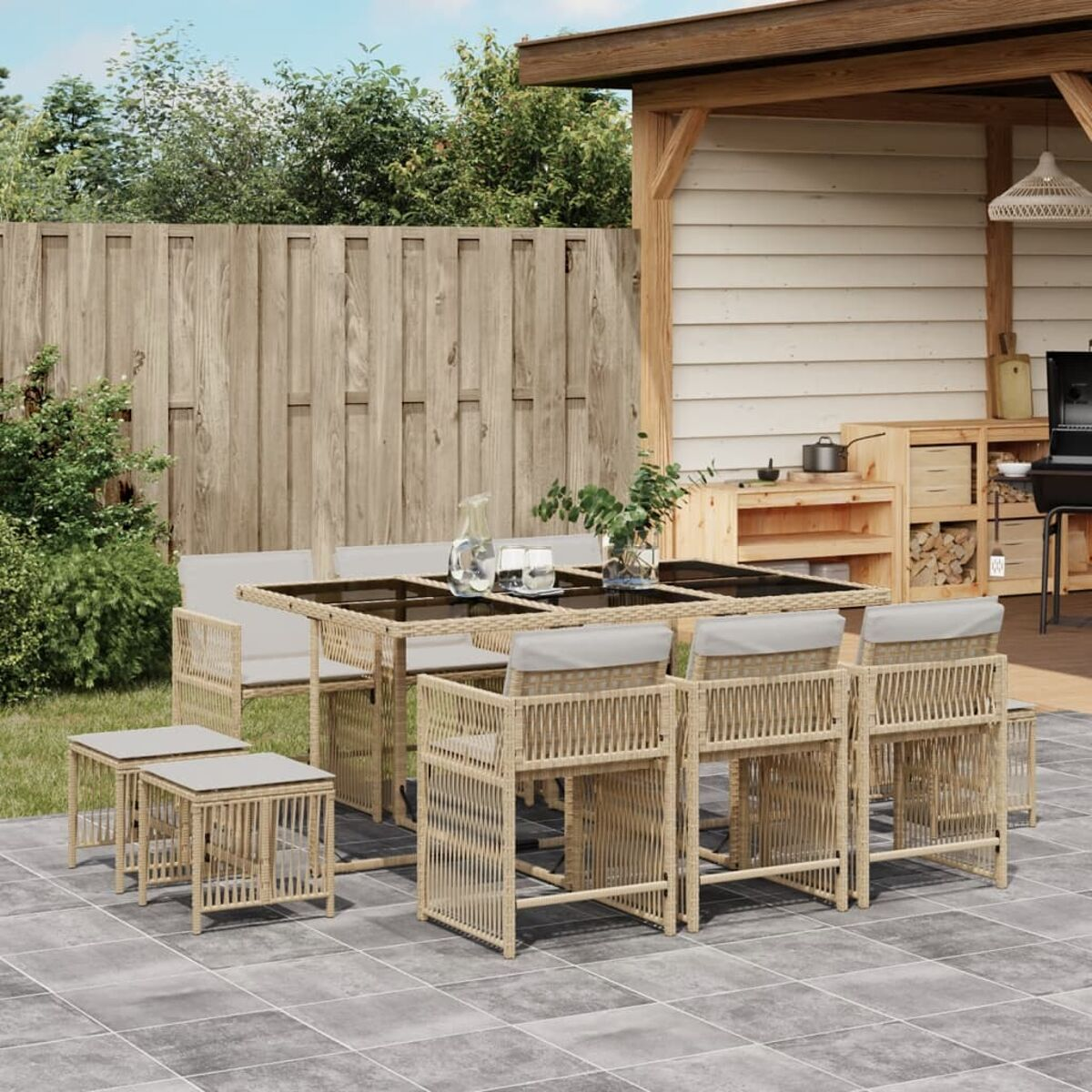 Set da pranzo all'aperto con tavolo e sedie su un patio piastrellato. Recinzione in legno e verde sullo sfondo.