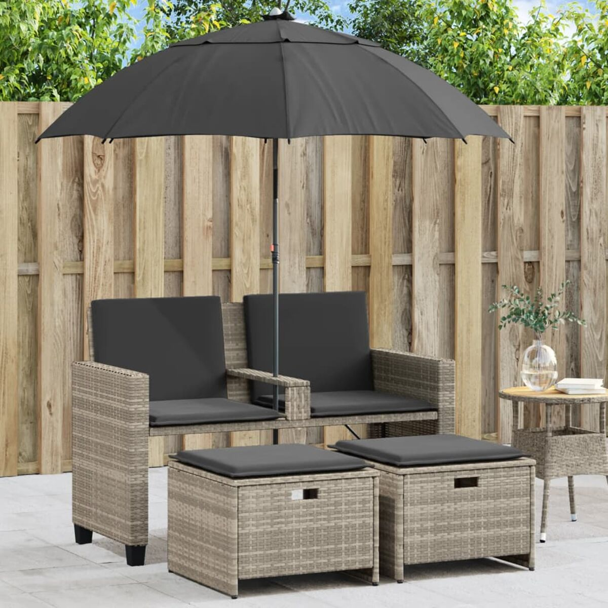 Set da patio con due sedie, due pouf e un ombrellone. Lo sfondo è una recinzione in legno.