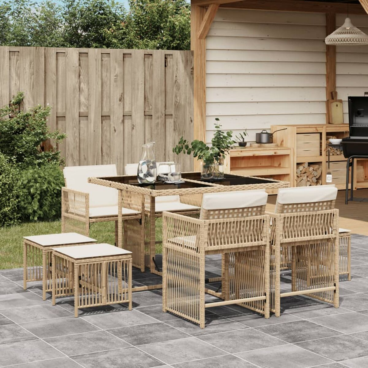 Set da pranzo all'aperto con tavolo, sedie e sgabelli; recinzione in legno e grill sullo sfondo.
