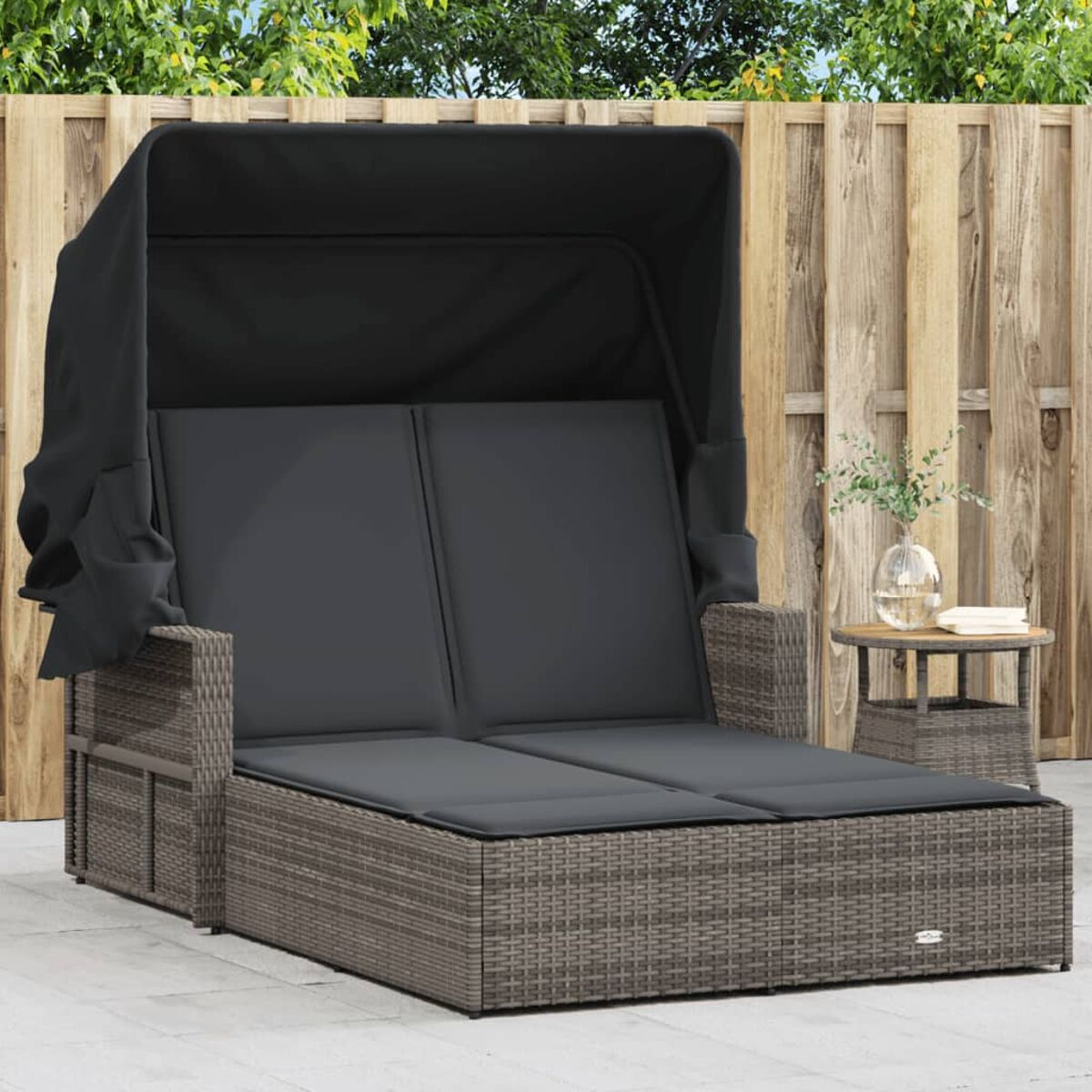 Rattan-Tagesbett mit Baldachin und grauen Kissen. Holzzaun im Hintergrund.