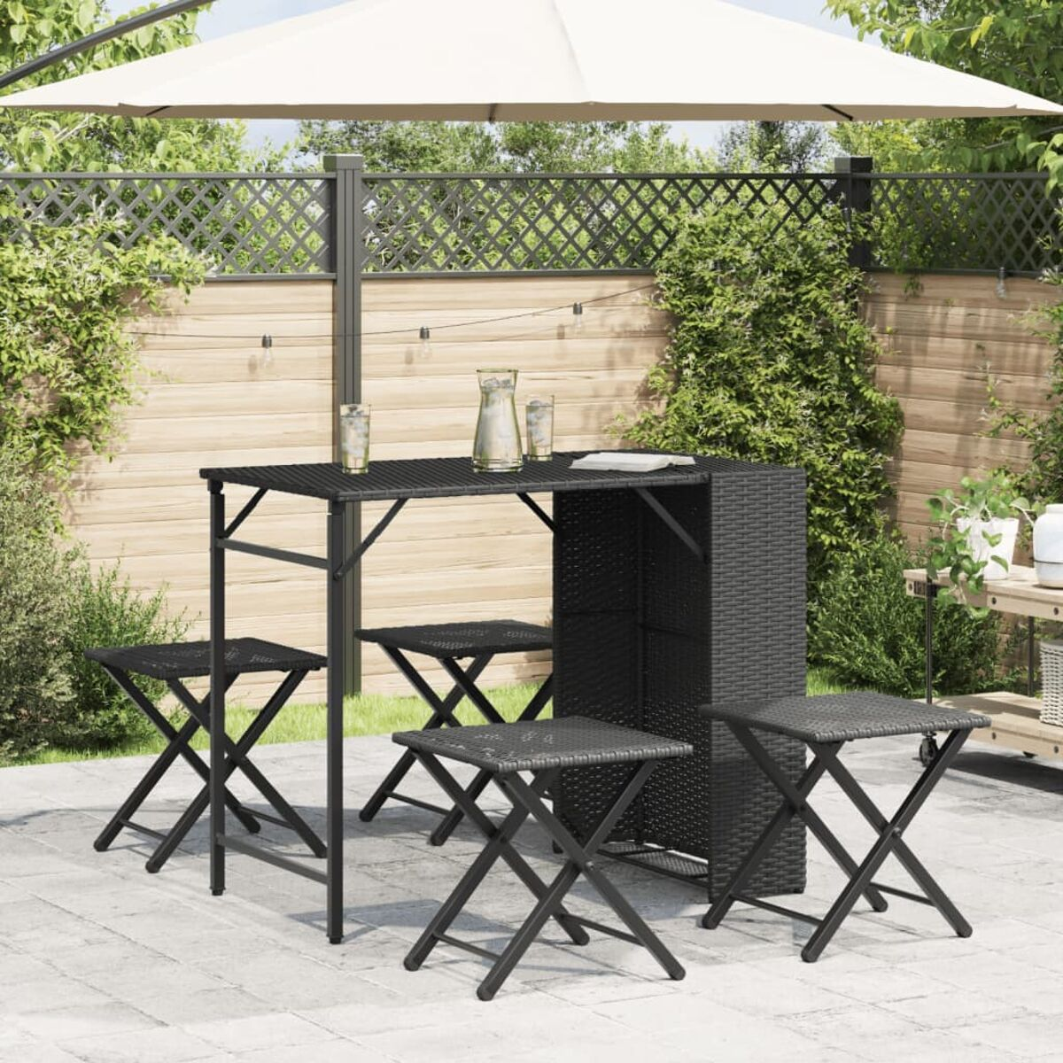 Ein schwarzes Bar-Set aus Korbgeflecht mit Tisch und Klapphockern unter einem Schirm.
