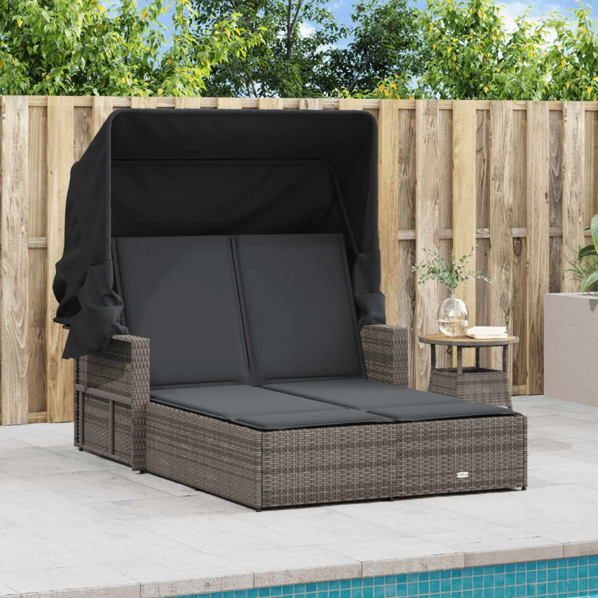 Ein graues Outdoor-Daybed mit schwarzem Verdeck steht auf einer Steinterrasse. Ein Beistelltisch steht daneben.