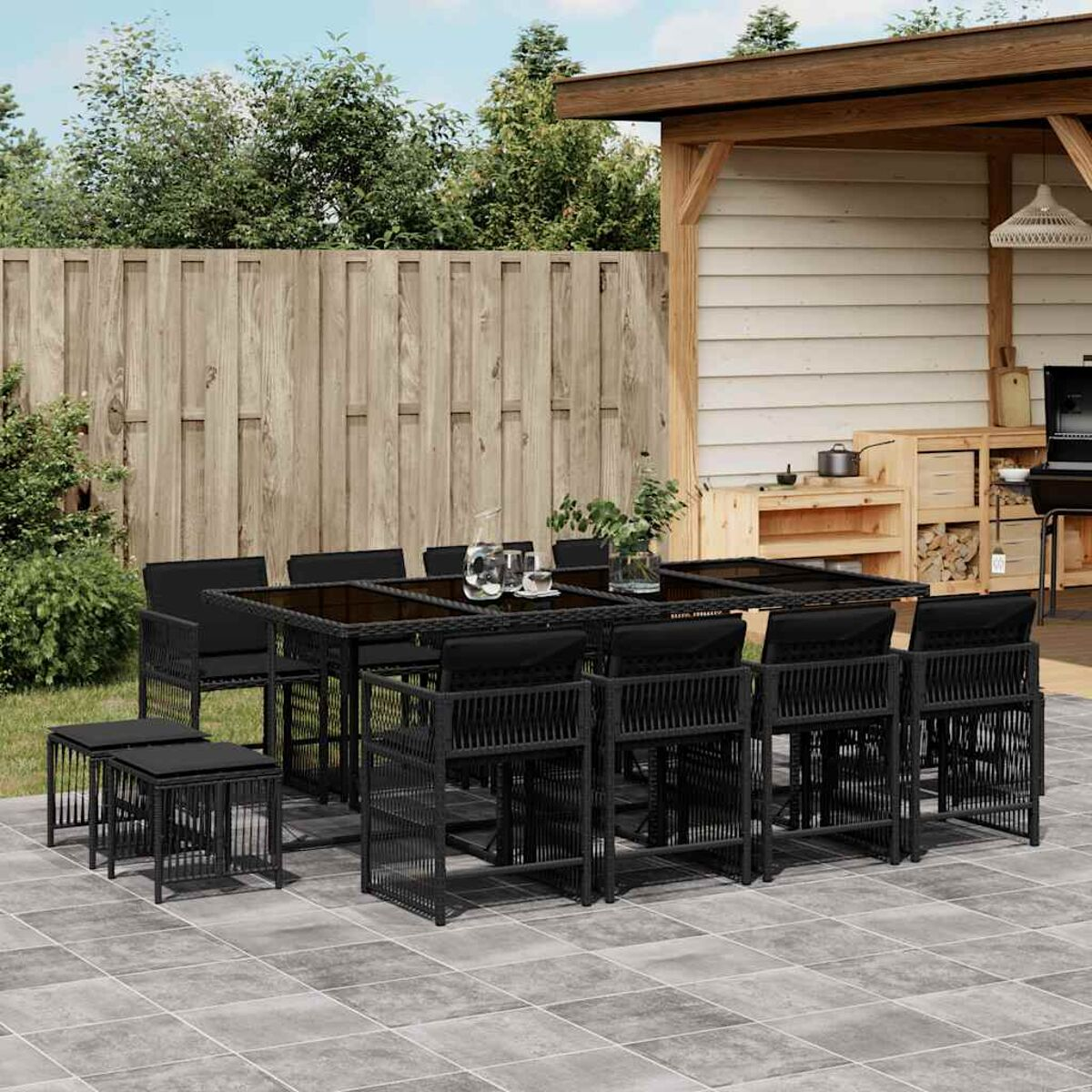 Set da pranzo all'aperto: tavolo con sedie. Su un patio con staccionata in legno e alberi.