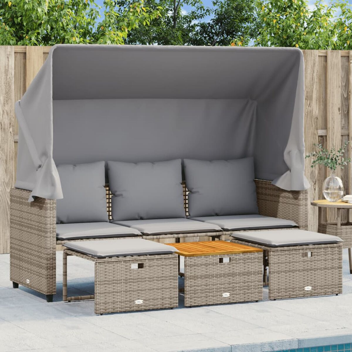 Divano in vimini con cuscini grigi, tendalino e tavolo in legno. Sono presenti pouf aggiuntivi.