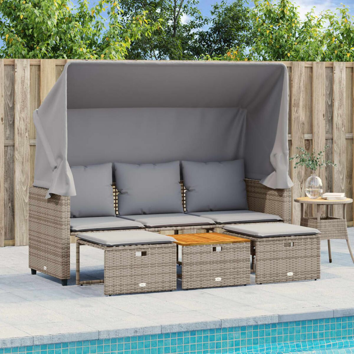 Divano esterno in vimini con cuscini. Tendalino grigio. Due pouf in vimini e un tavolo in legno. Piscina.