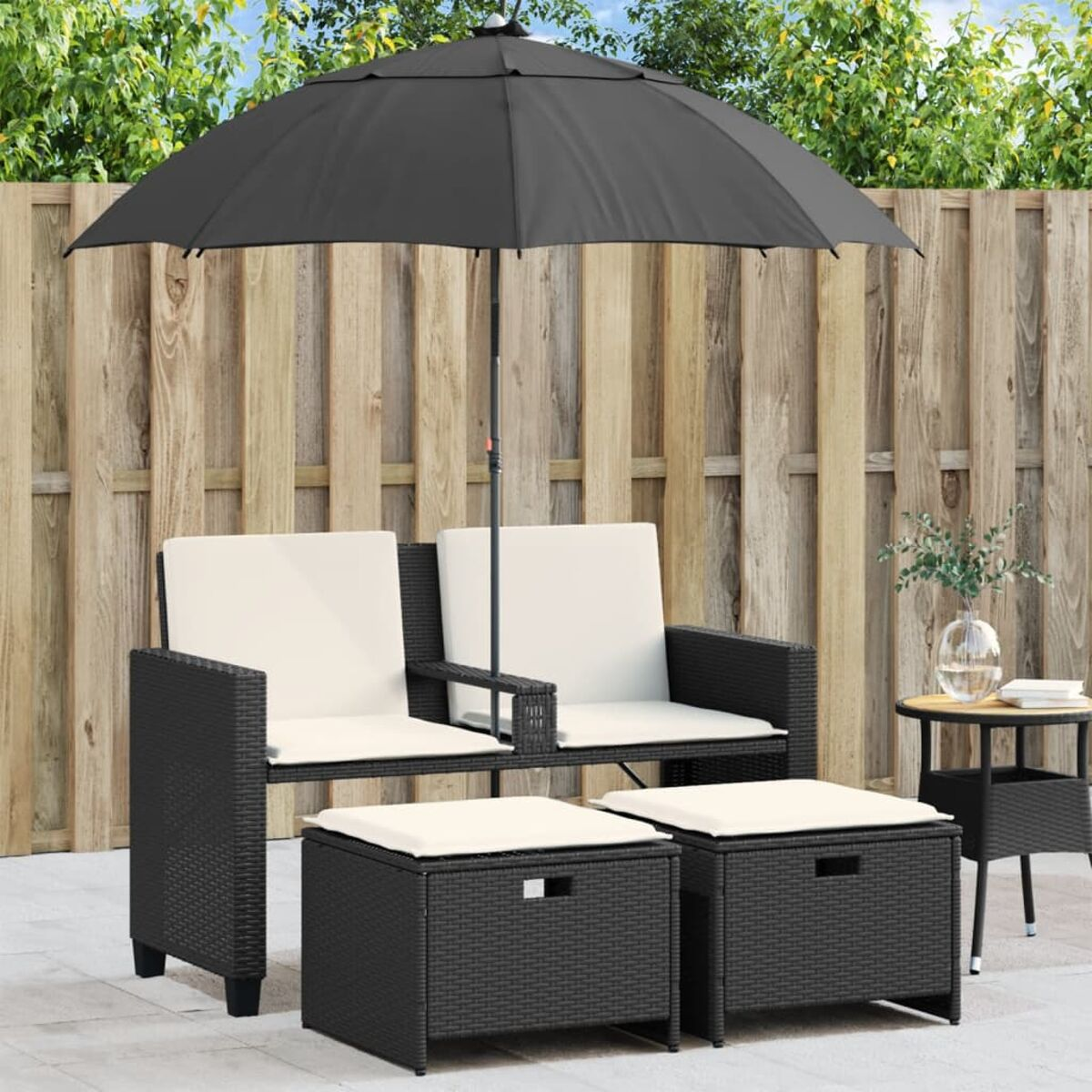 Set da salotto per esterni. Sedie e pouf in vimini nero con cuscini color crema. Ombrellone nero.