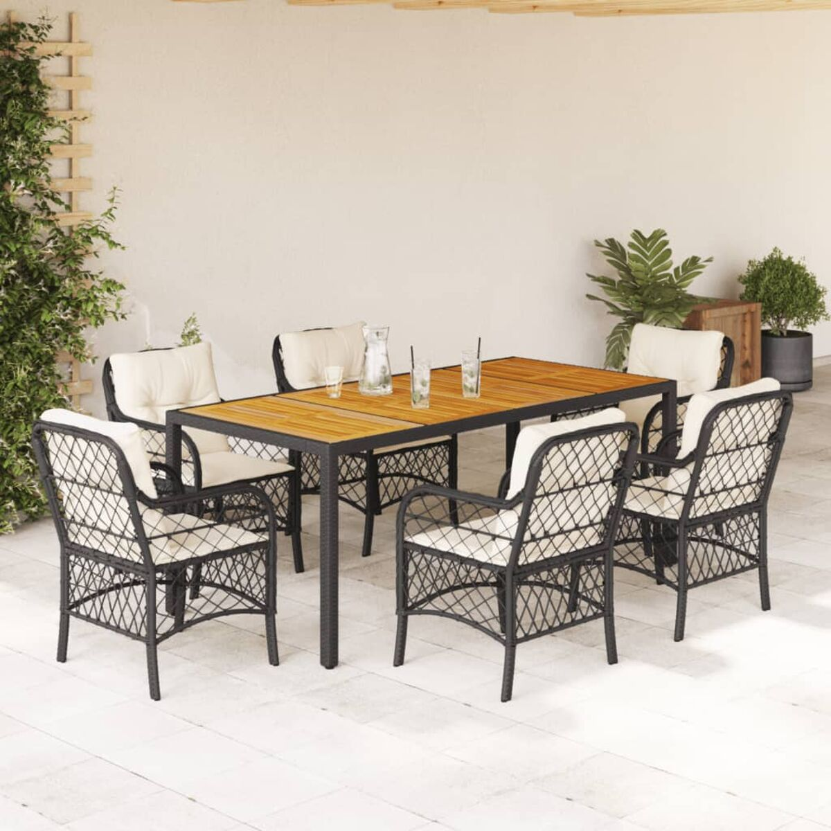 Set patio con tavolo in legno e sei sedie in vimini con cuscini. Piante sullo sfondo.