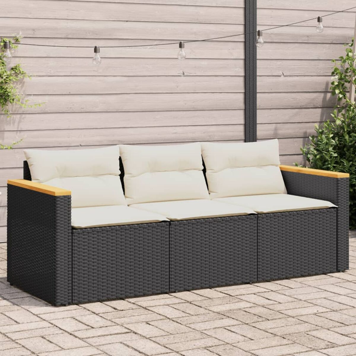 Ein schwarz-graues Outdoor-Sofa mit drei cremefarbenen Kissen. Es steht auf einer Ziegelterrasse.