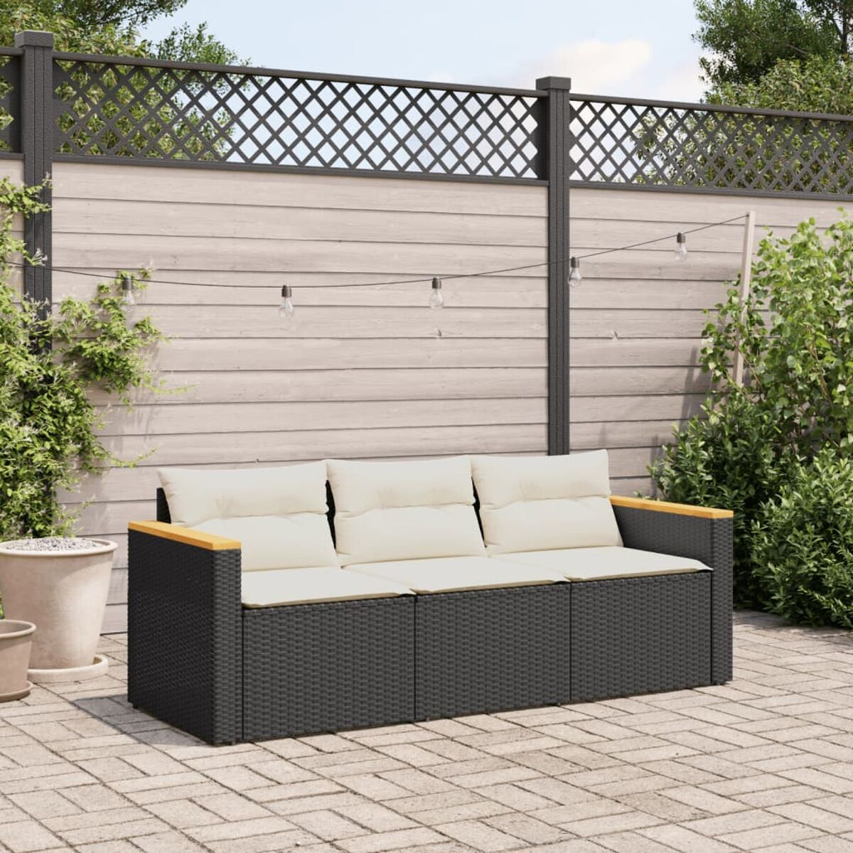 Ein dunkelgraues, gewebtes Outdoor-Sofa mit cremefarbenen Kissen, platziert auf einer Ziegelterrasse.