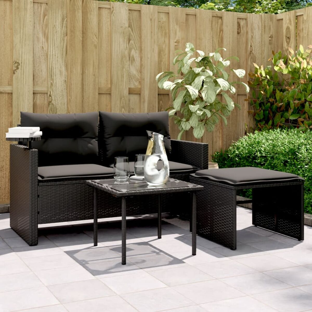 Set divano in rattan nero con cuscini, tavolino, bicchieri e caraffa d'acqua, all'aperto.