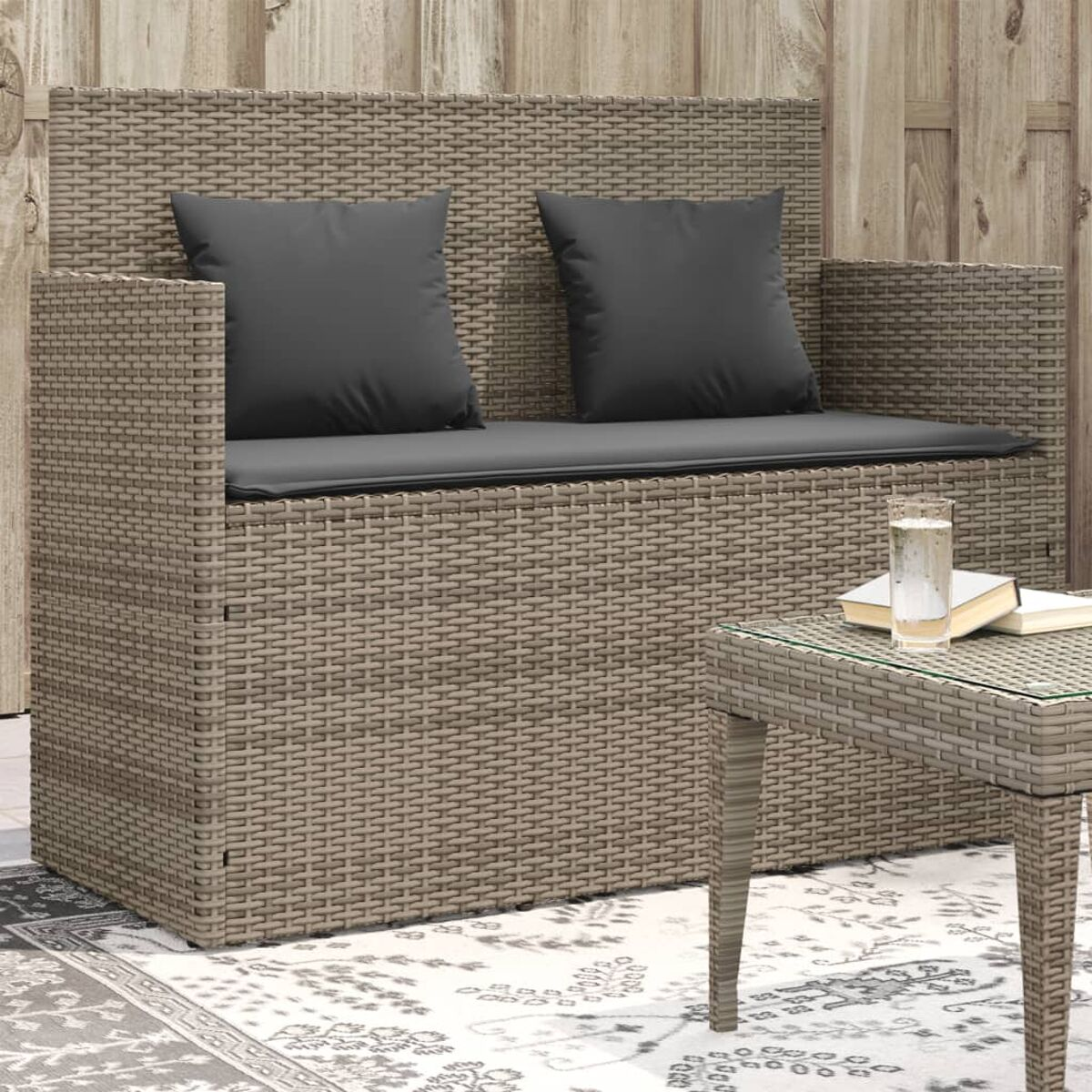 Geflochtene Liebescouch mit Kissen, kleiner Tisch mit Glas und Büchern auf Holzgrund.