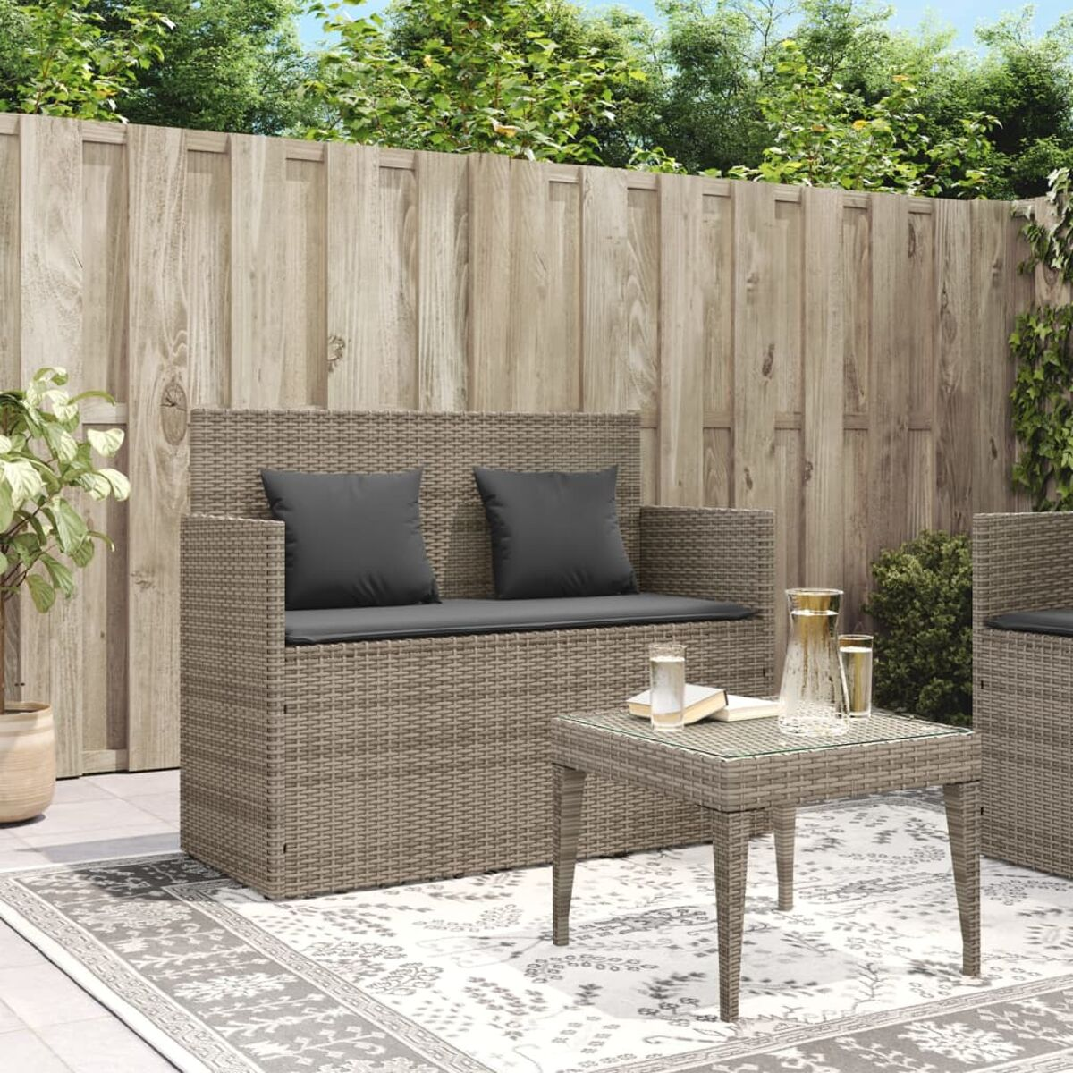 Graues Outdoor-Sofa aus Korbgeflecht mit zwei Kissen und passendem Couchtisch.