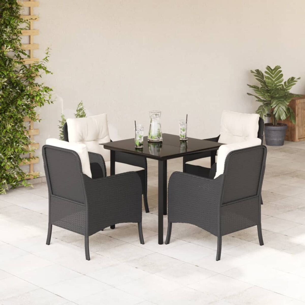 Terrassenset: schwarze Stühle mit weißen Kissen um einen schwarzen Tisch. Pflanzen und Spalier im Hintergrund.