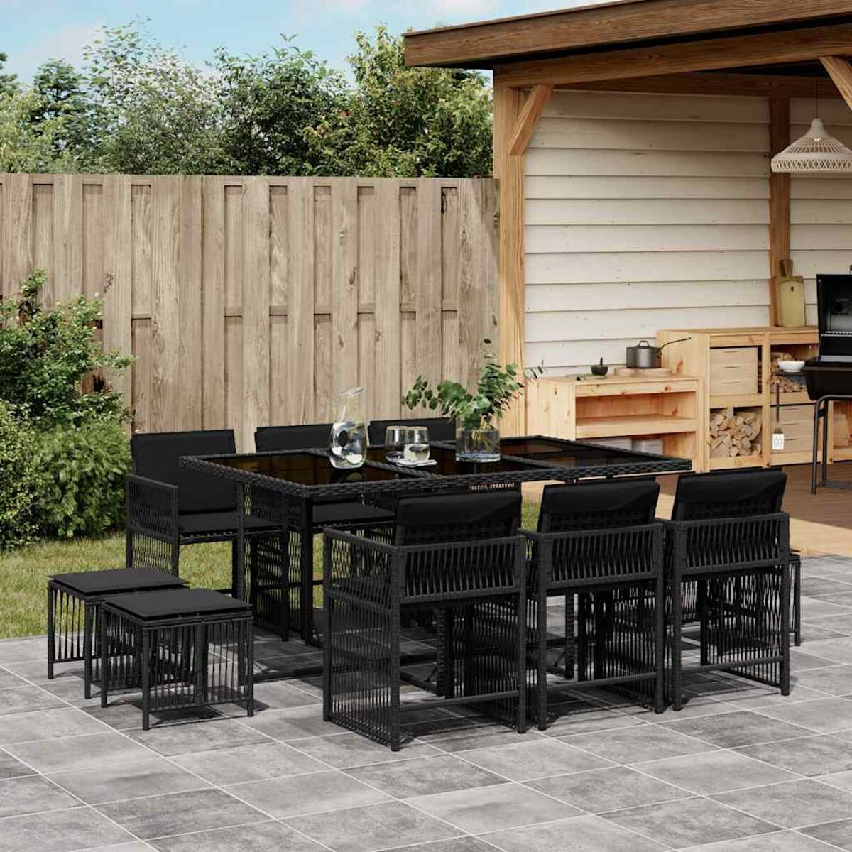 Set da pranzo esterno in vimini nero con tavolo e sedie su un patio piastrellato. Recinzione in legno sullo sfondo.