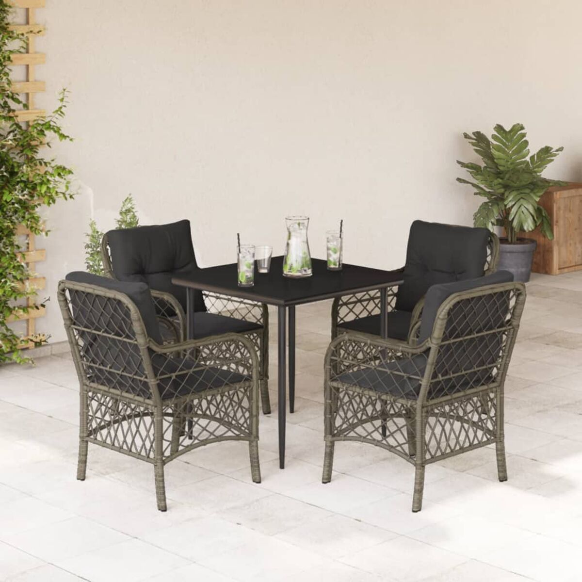 Terrassenset mit Tisch, vier Stühlen, Getränken und Pflanzen. Schwarze Kissen, graues Geflecht, heller Hintergrund.