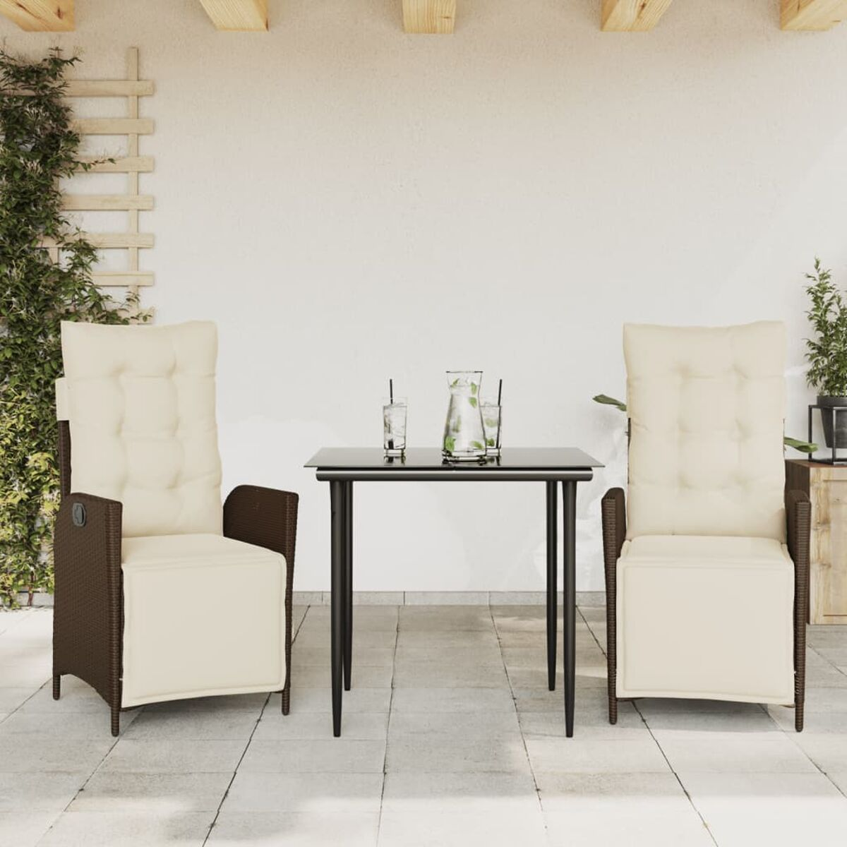 Set da patio: tavolo con 2 sedie, cuscini bianchi, design in vimini. Piante sullo sfondo.