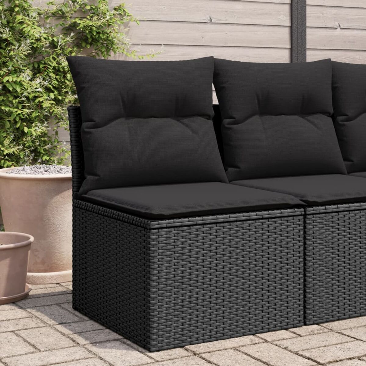 Schwarze Outdoor-Möbel aus Korbgeflecht mit Kissen. Auf einer Terrasse mit Grün im Hintergrund.