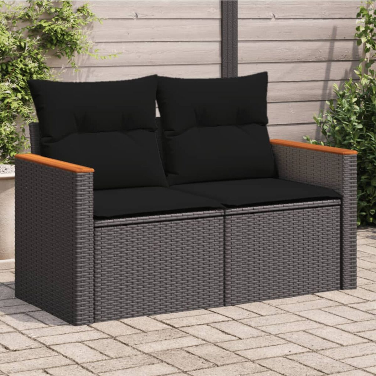 Ein graues Zweiersofa aus Korbgeflecht mit schwarzen Kissen auf einer Terrasse.