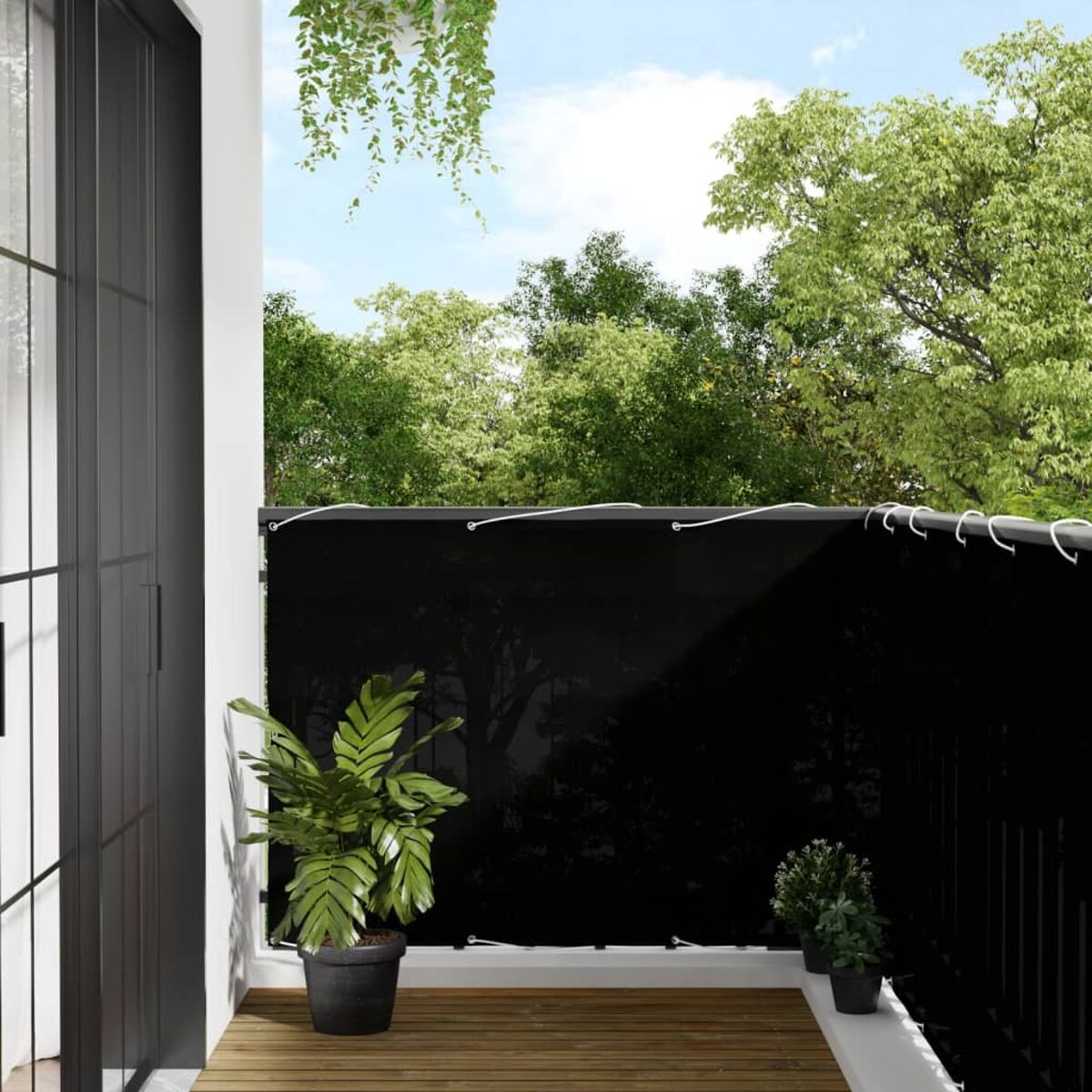Balkon mit schwarzem Sichtschutz, Pflanzen und Holzboden. Bäume und Himmel im Hintergrund.