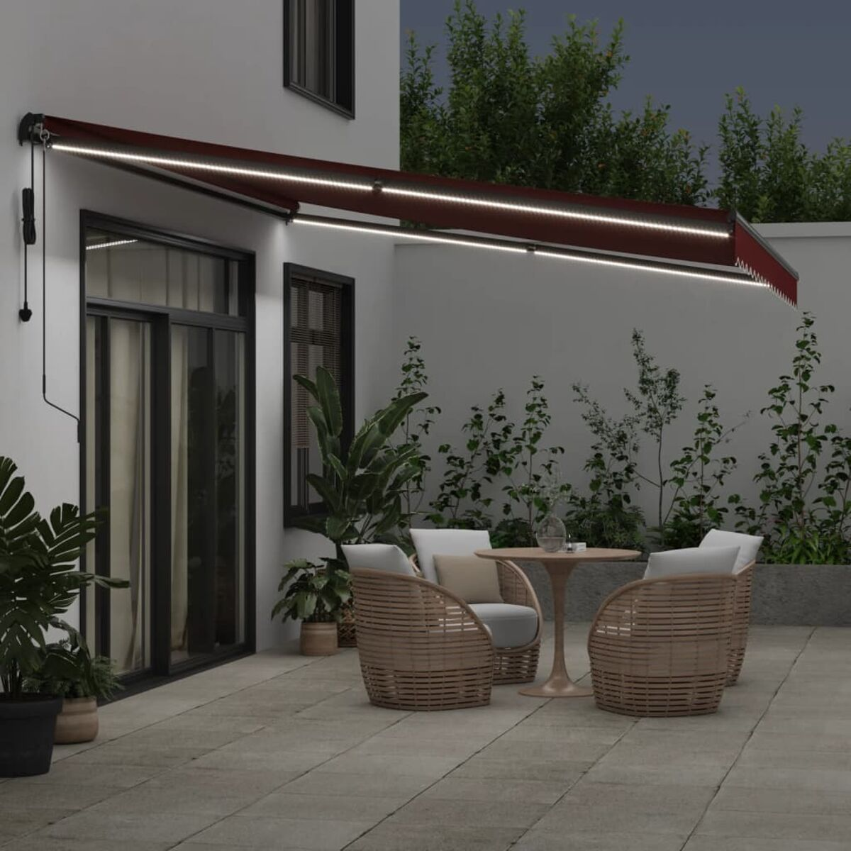 Terrasse mit Markise, Stühlen, Tisch und Pflanzen bei Nacht.