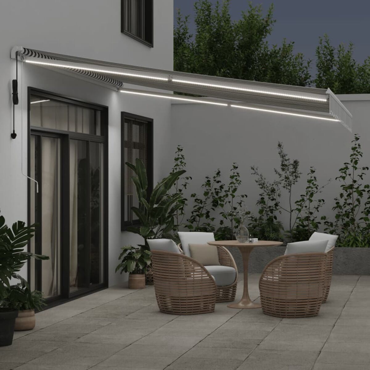 Eine Terrasse bei Nacht mit Markise, Stühlen und einem Tisch. Lichter über dem Sitzbereich.