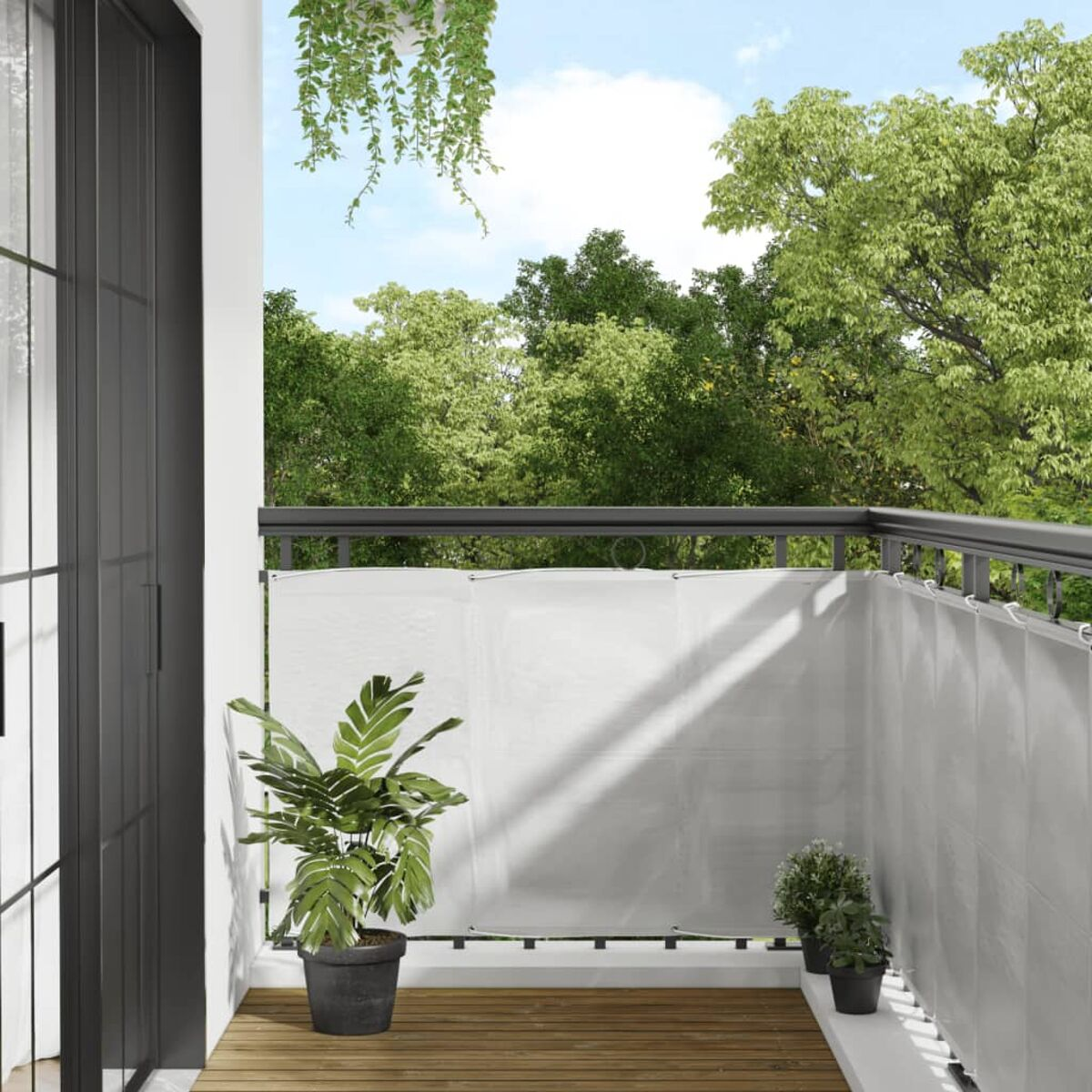 Balkon mit weißem Sichtschutz, Pflanzen in Töpfen und Bäumen im Hintergrund. Blauer Himmel.