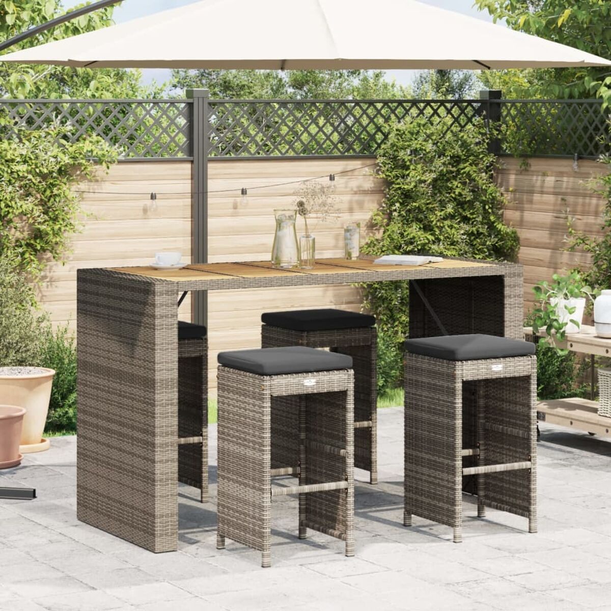 Outdoor-Bar-Set: Stehtisch und Hocker. Graues Weidengeflecht mit grauen Kissen. Sonnenschirm im Hintergrund.