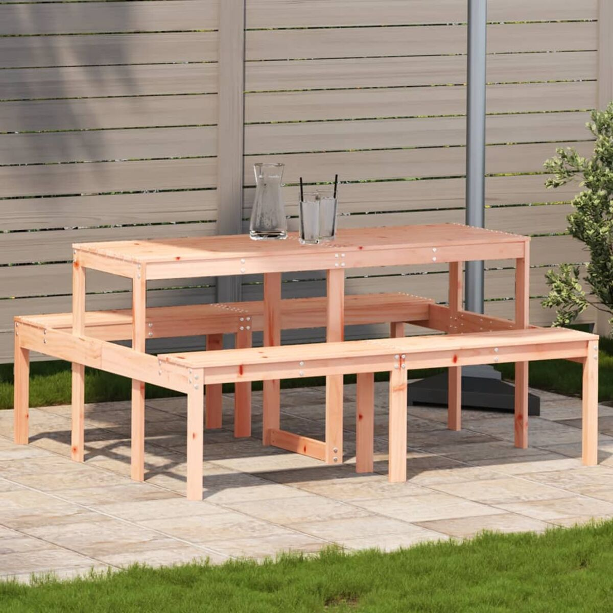 Holztisch und -bänke auf einer Terrasse. Gras und einige Bäume im Hintergrund.