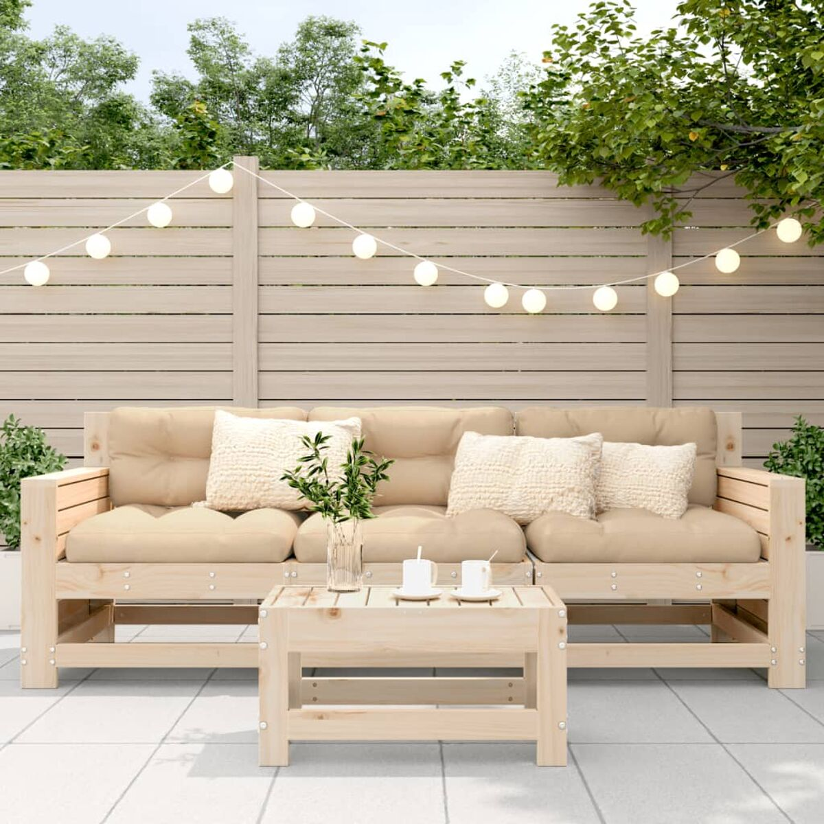 Ein helles Holzsofa und Tisch im Freien mit Kissen. Eine Lichterkette hängt darüber.