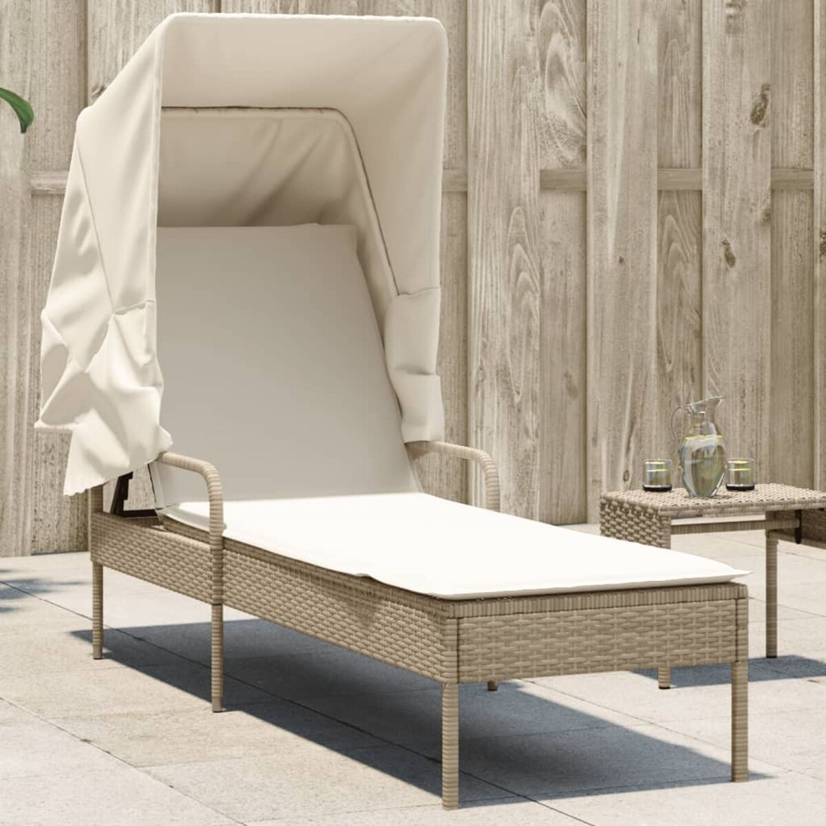 Sonnenliege aus Weide mit Baldachin. Beige, kleiner Beistelltisch und Holzzaun im Hintergrund.