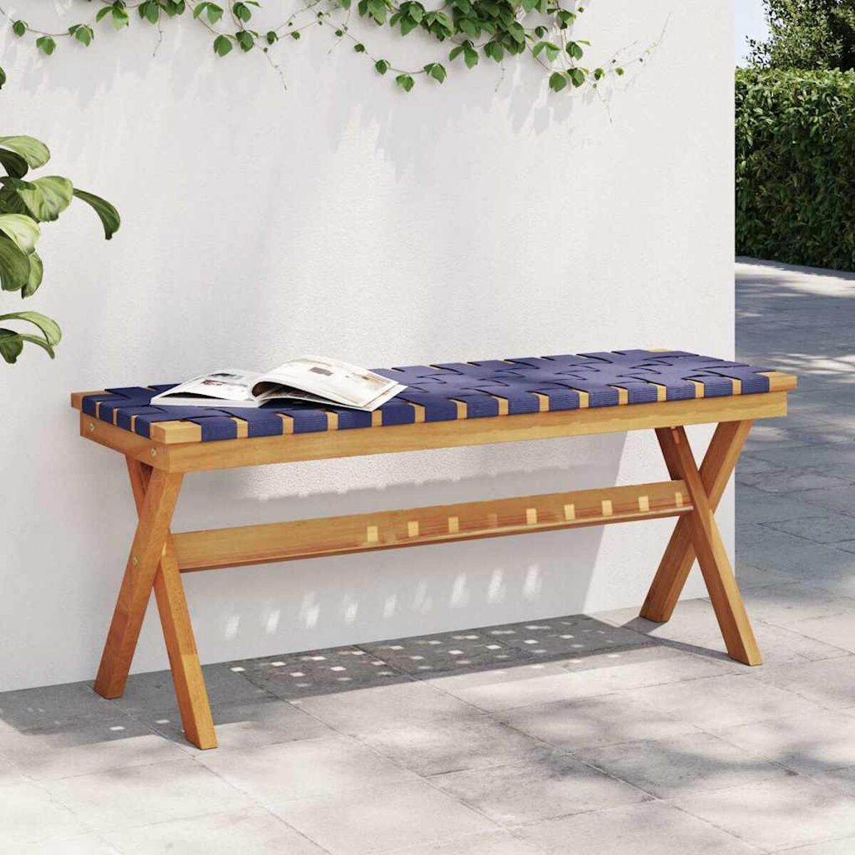 Panca in legno con seduta blu intrecciata, libro sopra, contro muro bianco.