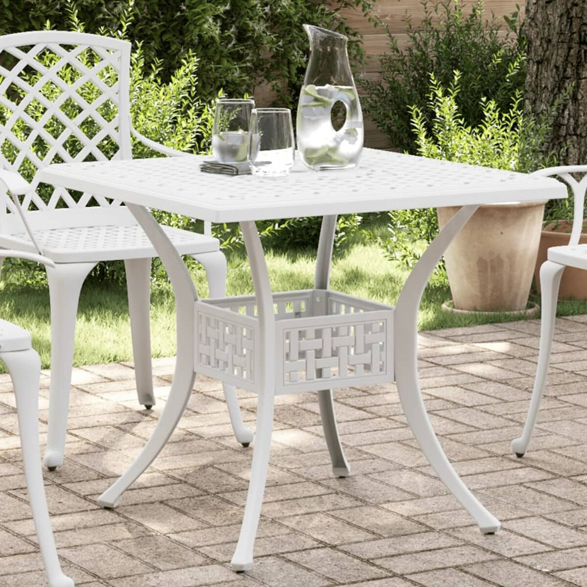 Weißes Outdoor-Ess-Set mit quadratischem Tisch und Stühlen. Krug und Gläser stehen auf dem Tisch.