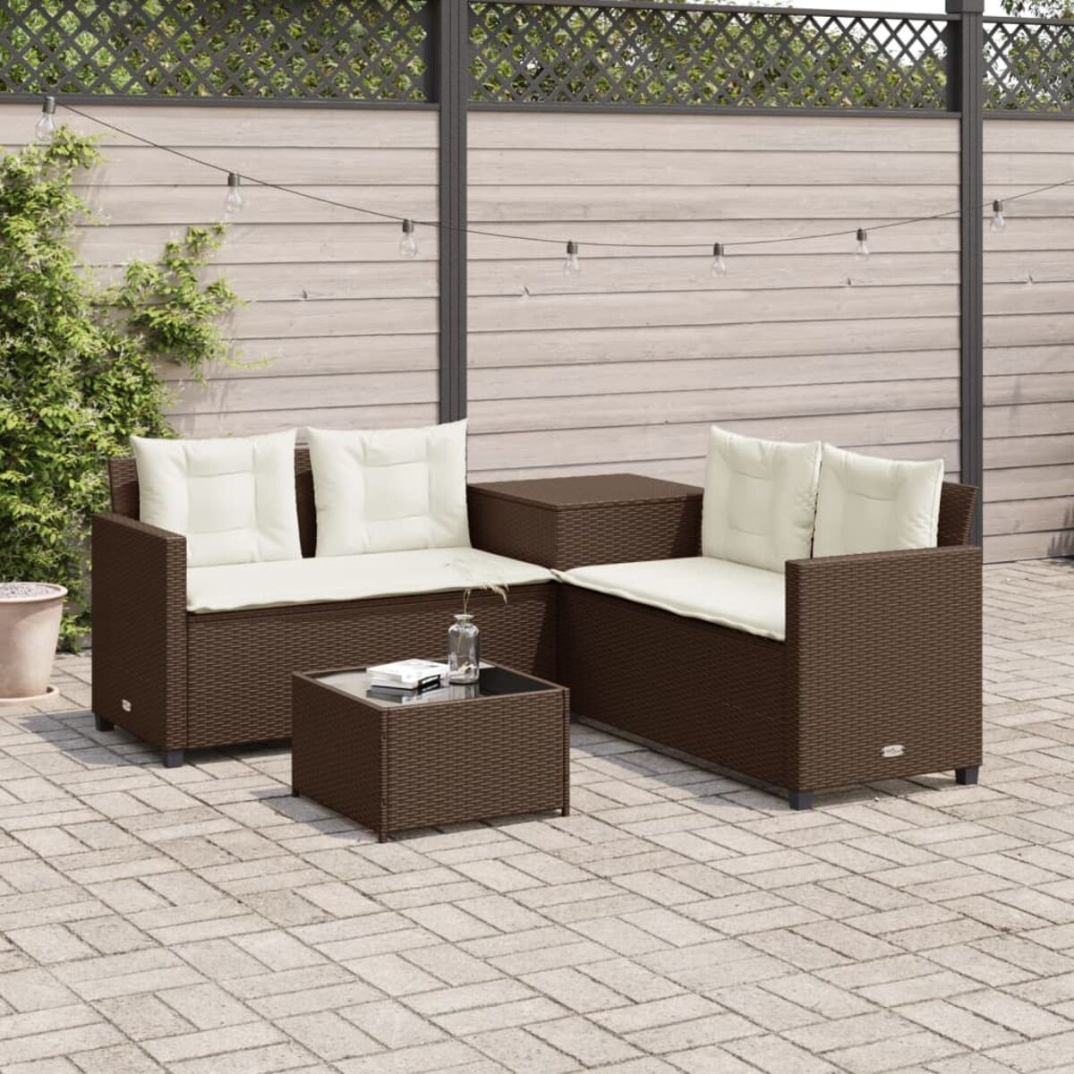 Set divano da esterno in rattan marrone con cuscini color crema e tavolo in vetro su un patio.
