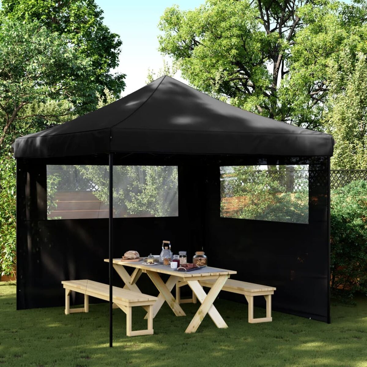 Schwarzes Zelt mit Picknicktisch und Bänken im Inneren. Der Hintergrund ist ein Garten.