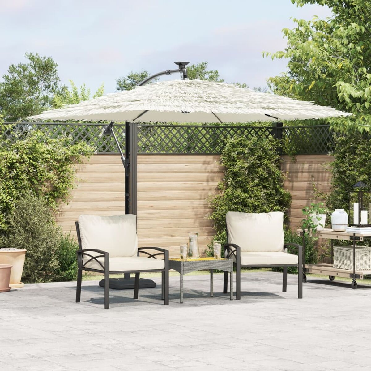 Terrassenset mit cremefarbenen Kissen und großem Schirm. Bäume und ein Zaun im Hintergrund.