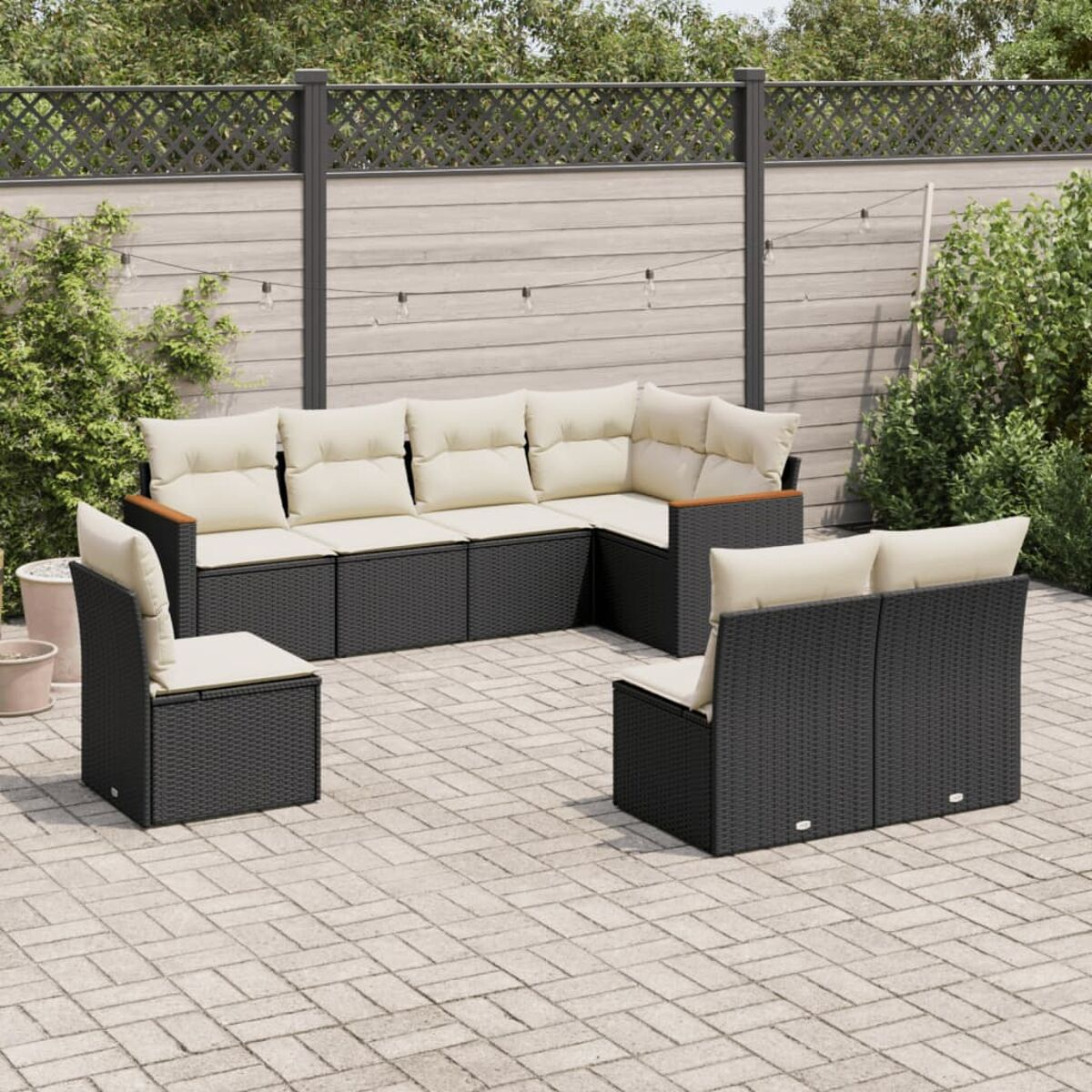 Ein schwarzes Outdoor-Möbelset aus Korbgeflecht mit cremefarbenen Kissen auf einer gepflasterten Terrasse.