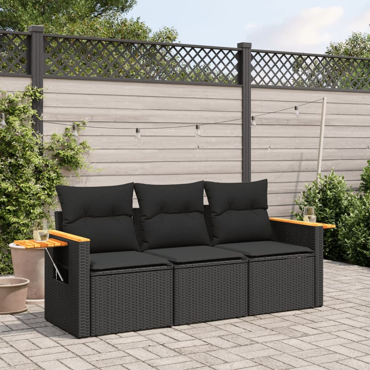 Ein schwarzes, gewebtes Outdoor-Sofa mit schwarzen Kissen und Holzarmlehnen auf einer Terrasse.