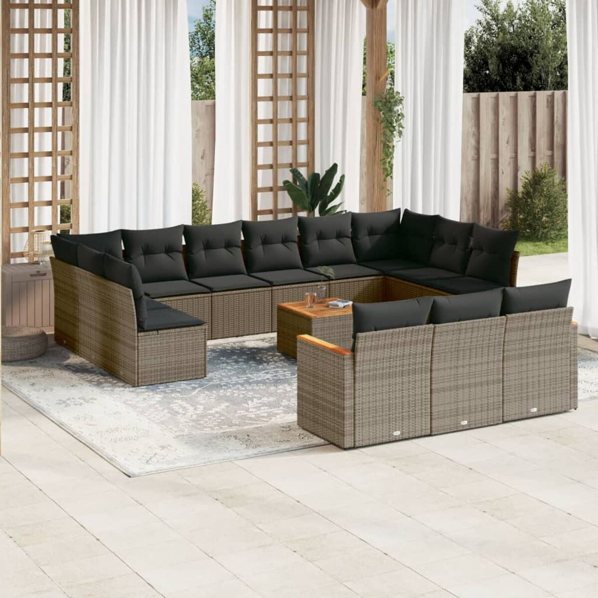 Ein U-förmiges Outdoor-Sofa aus Rattan mit schwarzen Kissen auf einem Teppich. Die Szene ist auf einer Terrasse.
