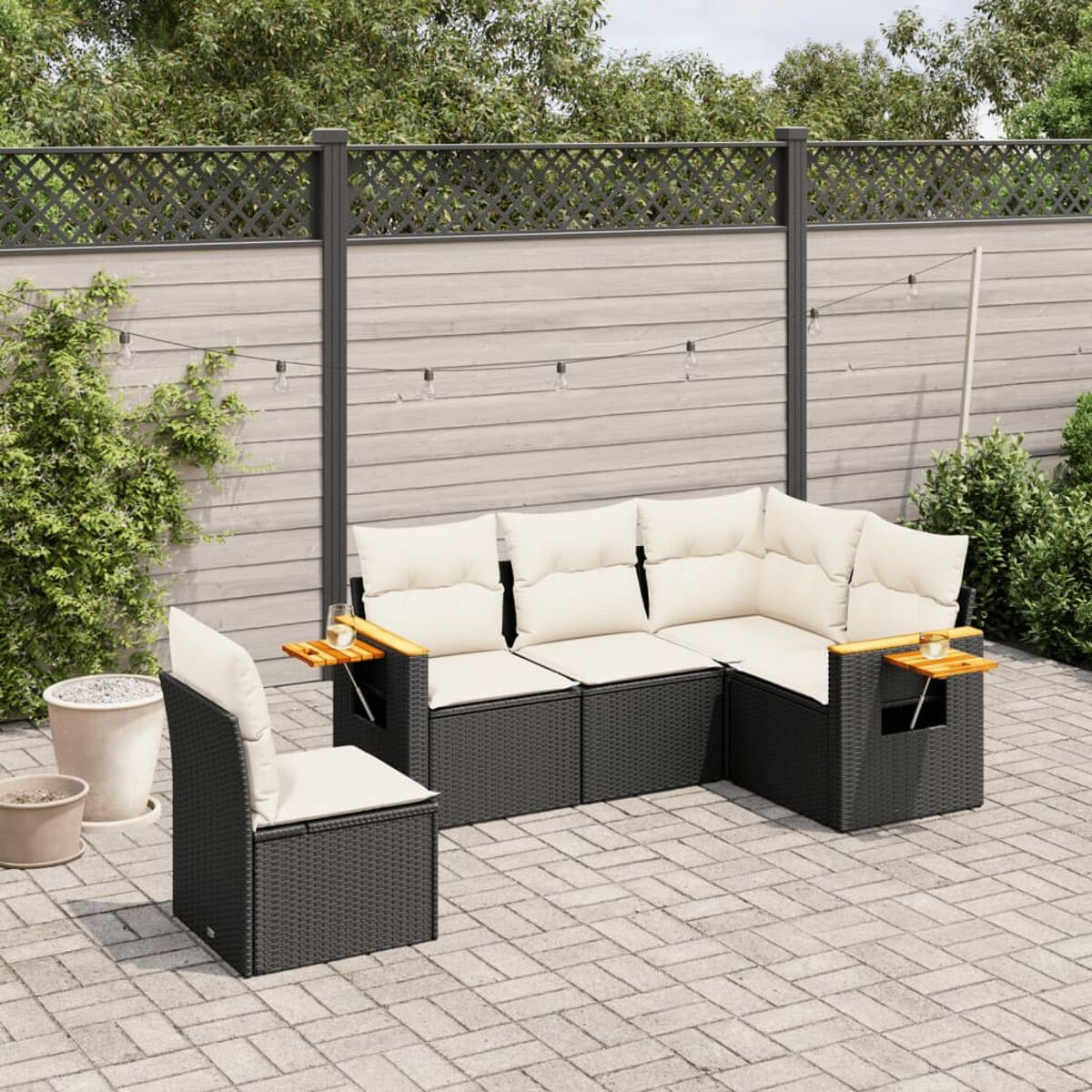 Schwarzes Outdoor-Geflecht-Ecksofa-Set mit beigen Kissen auf einer gepflasterten Terrasse mit Zaun.