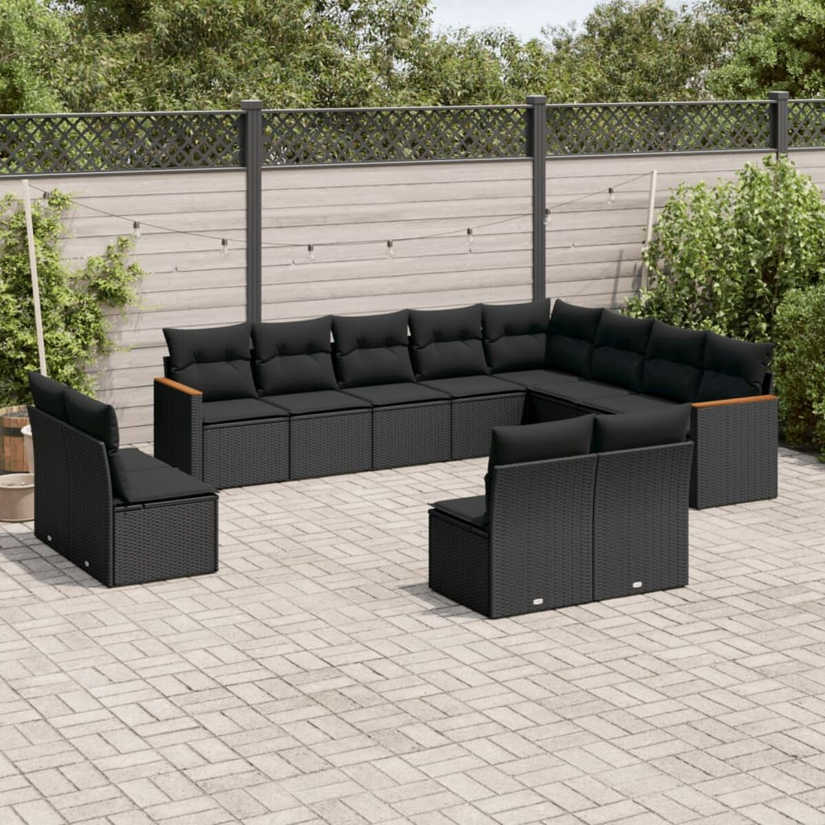 Schwarzes Outdoor-Korbmöbel-Set. Enthält Ecksofa, Stühle und Kissen. Holzzaun im Hintergrund.