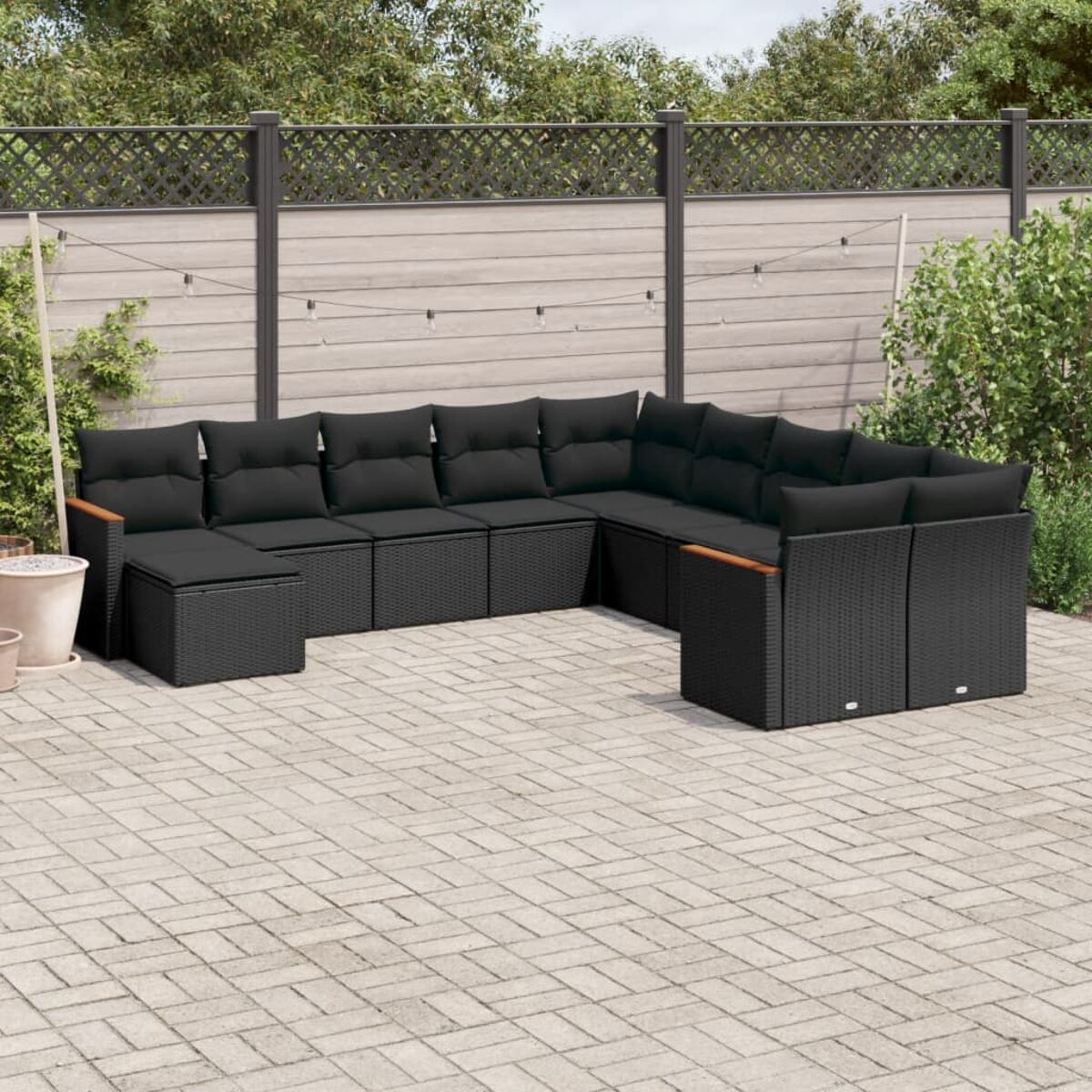Ecksofa für den Außenbereich mit schwarzen Kissen auf einer Terrasse. Im Hintergrund Zaun und Pflanzen.