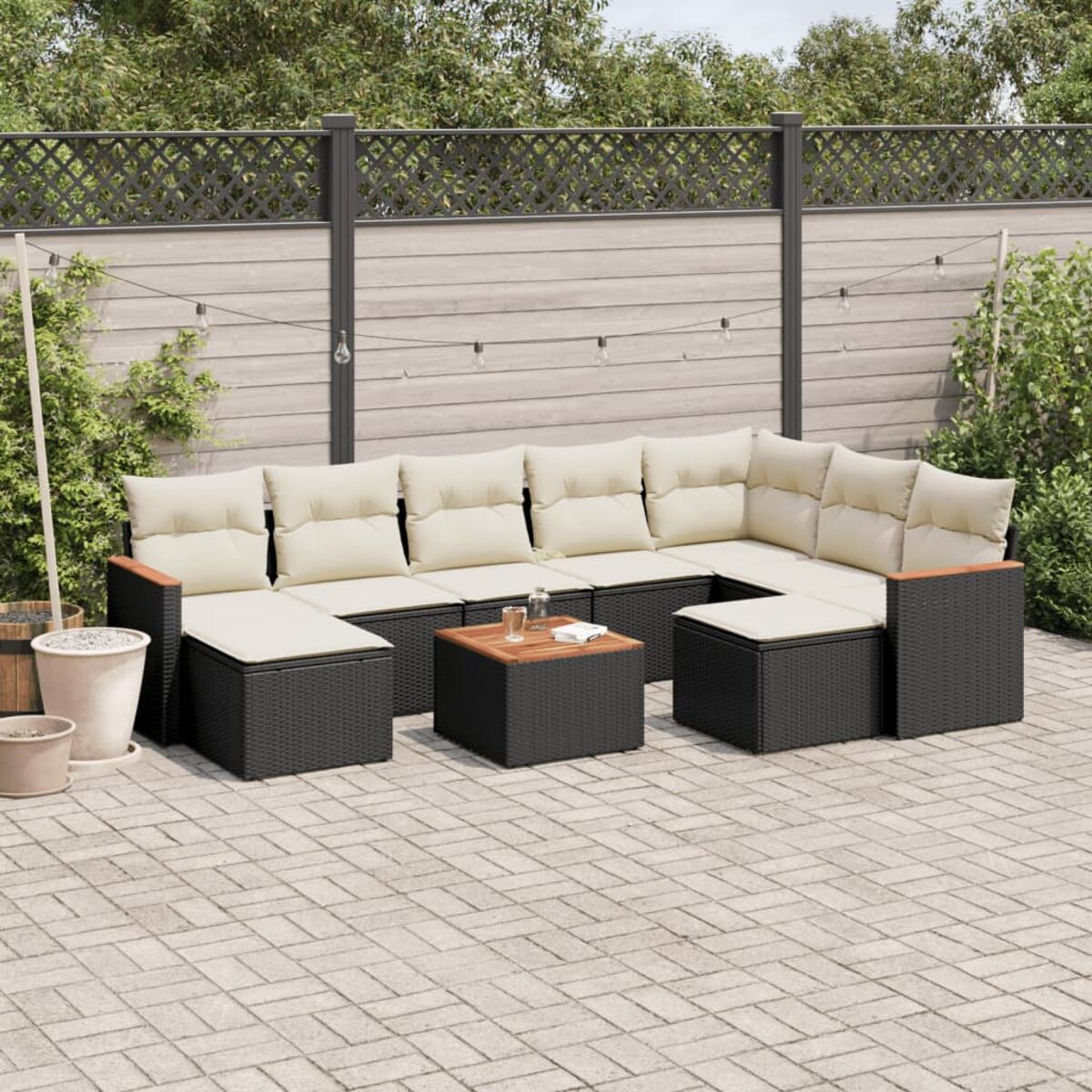 Schwarzes Outdoor-Ecksofa aus Korbgeflecht mit beigefarbenen Kissen auf einer Backstein-Terrasse.