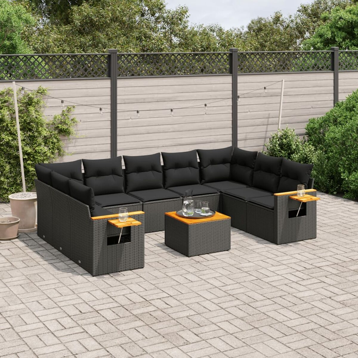 Geflochtene Outdoor-Eckcouch mit schwarzen Kissen, Holzarmlehnen und Couchtisch. Zaun und Lichter.